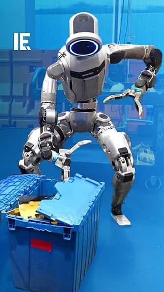 Atlas, configured for material handling, lifting a part from a logistics crate. Production has begun, with early units allocated to autonomous material handling at Hyundai's Metaplant America. The labor is the machine's; the judgment is not.